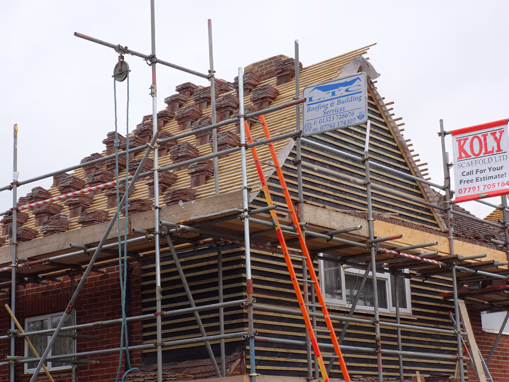 Scaffolding surrounds a house under construction, with workers installing roofing materials.